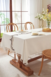Detailed close-up of leaf embroidery and fringe edges on a cream linen tablecloth
