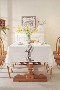 Detail of leaf embroidery and white fringe tassels on a beige linen tablecloth