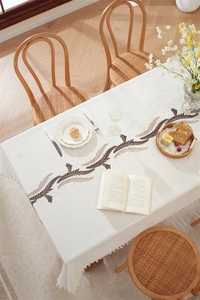 Close-up of beige linen tablecloth with brown wheat embroidery and white tassel fringe