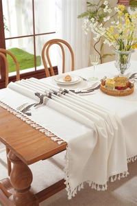 Detail of embroidered leaves and fringe tassels on a cream cotton linen tablecloth