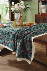 Close-up of vintage floral jacquard tablecloth with deep green base and cream tassels