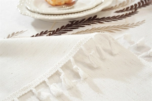 Close-up of embroidered leaf patterns and white fringe tassels on linen tablecloth