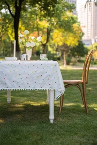 Detail of white cotton tablecloth with geometric embroidery and white pom-pom fringe
