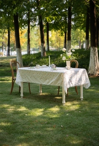 Detailed close-up of white cotton tablecloth with geometric embroidery and pom-pom fringe