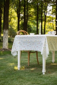 Close-up of geometric embroidery and white pom-pom fringe on a cotton tablecloth