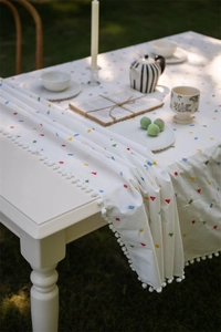 Detail of white cotton tablecloth featuring colorful geometric embroidery and pompom fringe
