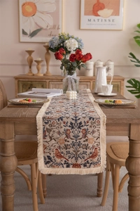 Macro detail of vintage floral table runner with tassel edges on a dark wood dining table