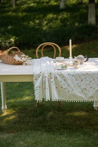 Close-up of white cotton tablecloth featuring colorful geometric embroidery and pompom edges