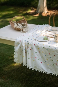 Detail of cotton tablecloth featuring geometric embroidery and white pom pom lace trim