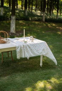 Close-up of white cotton tablecloth with geometric floral print and pom-pom trim detail