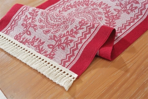 Detail of red and white jacquard table runner with vintage floral patterns and tassels