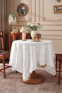 Close-up of white cotton tablecloth with floral jacquard and ruffled lace hem detail