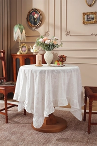 Detailed view of white cotton tablecloth featuring embroidered lace and ruffled edges
