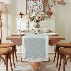 Teal jacquard table runner with white geometric patterns and tassel details on a wooden table