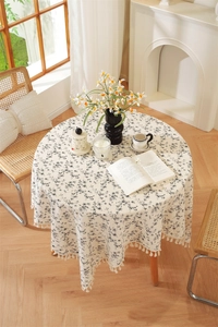 Macro detail of round floral cotton tablecloth with tassel fringe on a wooden table