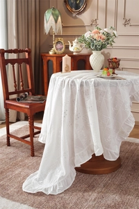 Close-up of white cotton tablecloth with floral embroidery and ruffled lace edge