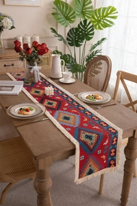 Close-up of red bohemian geometric table runner with intricate white tassels on a wood table