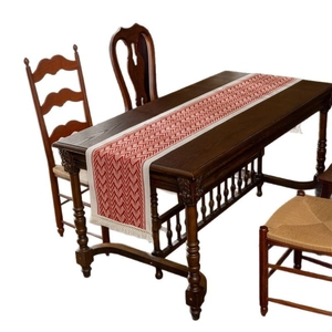 Red and cream geometric wave pattern table runner with tassels on dark wood table