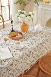 Close-up of cream floral cotton tablecloth with fringe tassels and woven texture
