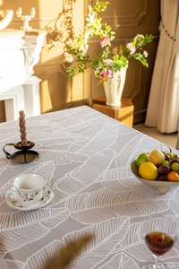 Close-up of lace tablecloth with white leaf patterns and rustic linen texture