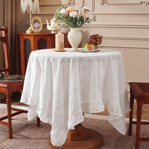 White cotton tablecloth with floral embroidery and ruffled edges on round table