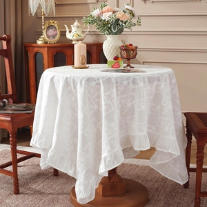 White cotton lace tablecloth with geometric embroidery and ruffled edges on round table