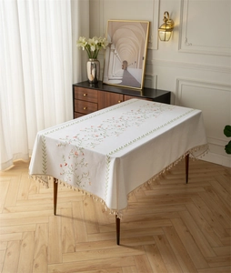 Close-up of elegant floral embroidery and beige tassels on a white linen tablecloth