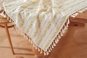 Close-up of floral cotton tablecloth featuring delicate yellow flowers and white fringe