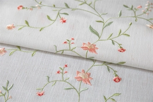 Close-up of floral embroidery on white linen textured tablecloth with fringe details