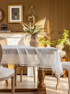 Detail of white lace tablecloth with leaf patterns and fringe in a vintage setting