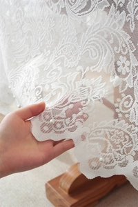 Dettaglio di tovaglia in pizzo bianco con ricami floreali e delicate perle bianche