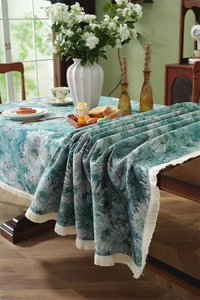 Detailed view of jacquard floral patterns and white fringe tassels on teal tablecloth