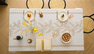 Detailed view of beige linen texture tablecloth with yellow floral embroidery and fringe