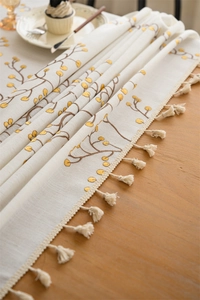 Detail of embroidered yellow berry pattern on a beige table runner with tassels