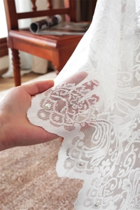 Primo piano di una tovaglia in pizzo bianco con motivi floreali e decorazioni in perle