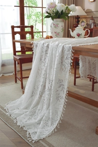 Close-up of white lace table runner with leaf pattern, floral jacquard and tassel edge