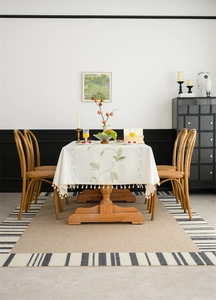 Detail of embroidered green vine patterns and tassel fringe on beige rectangular tablecloth