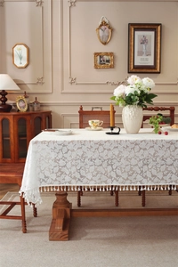 Detailed texture of white lace tablecloth with leaf patterns and fringe tassels on wood table