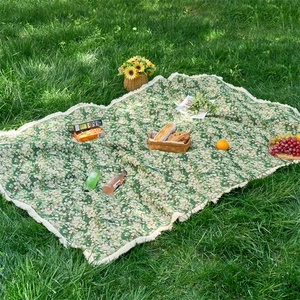 Close-up of green floral jacquard picnic mat featuring white fringe trim on lush grass