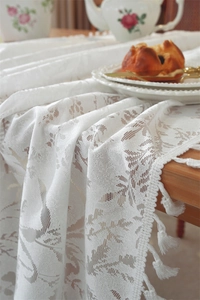 Close-up of white lace tablecloth with floral leaf patterns and elegant cotton tassels