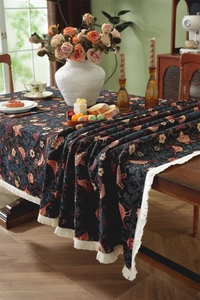Detail of floral jacquard tablecloth with white tassels on vintage wooden dining table