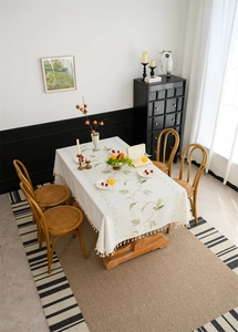 Detailed close-up of cream rectangular tablecloth with green floral embroidery and fringe