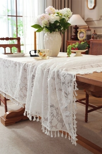Detail of white lace tablecloth featuring floral hollow patterns and tassel fringe edges