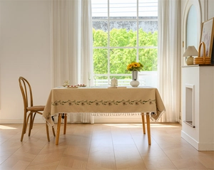 Detail of beige rectangular tablecloth with floral embroidery and white fringe edges