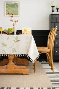 Detail of embroidered beige tablecloth with green leaf patterns and cream tassel edges
