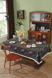 Close-up of vintage dark green floral tablecloth with white tassels on a wooden table