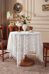 Detailed close-up of white lace tablecloth with leaf patterns and fringe tassels