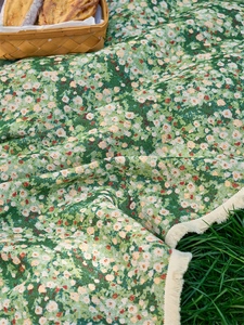 Detail of green floral picnic mat with tassels on grass next to a bread basket