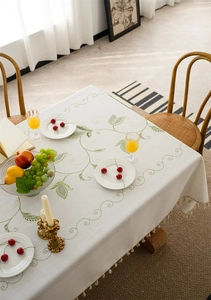 Close-up of embroidered green leaf pattern and decorative ball fringe on cream tablecloth