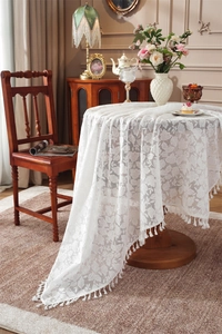 Detailed view of white floral lace tablecloth featuring leaf patterns and fringe tassels
